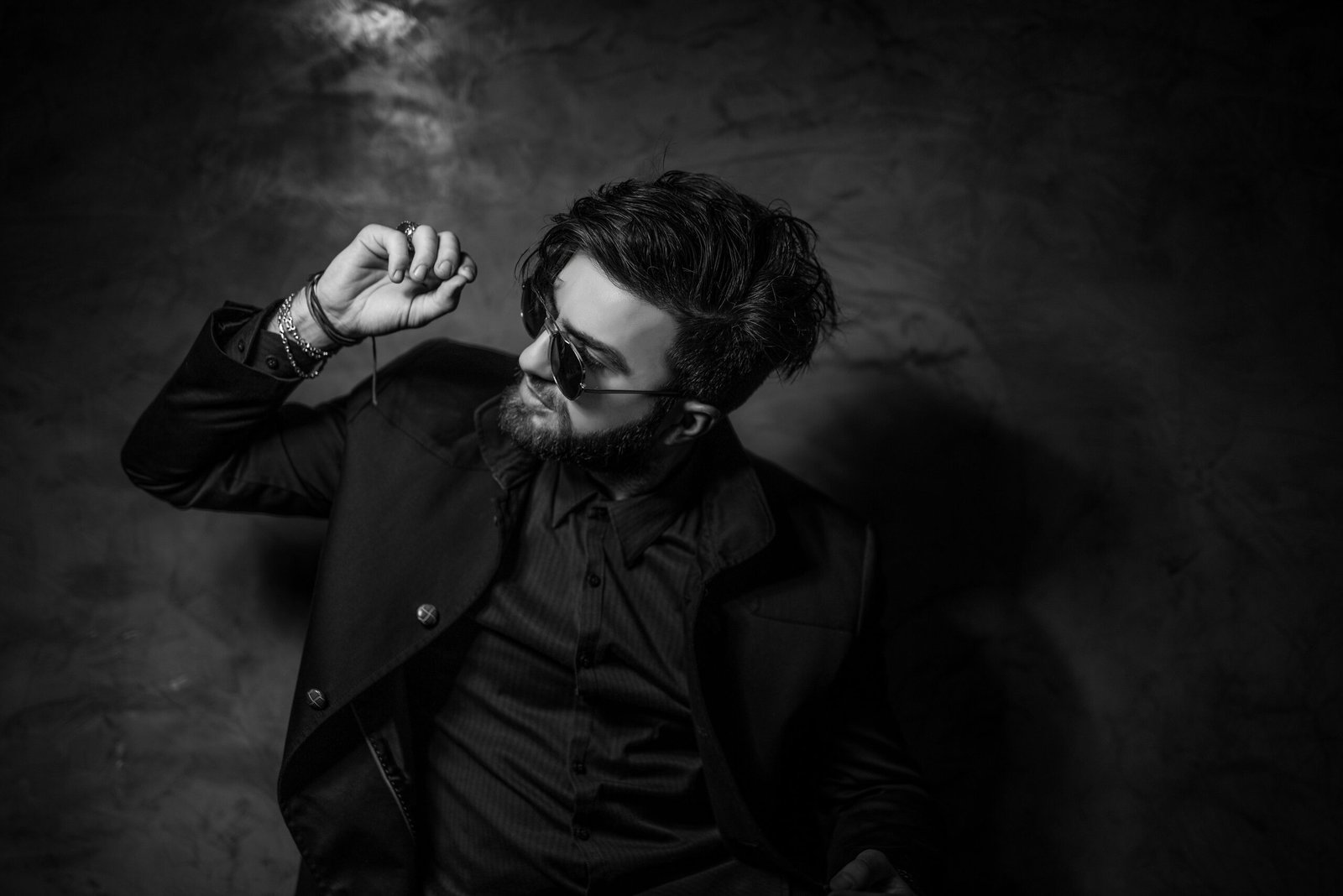 Black and white portrait of a fashionable man in sunglasses and suit posing confidently indoors.